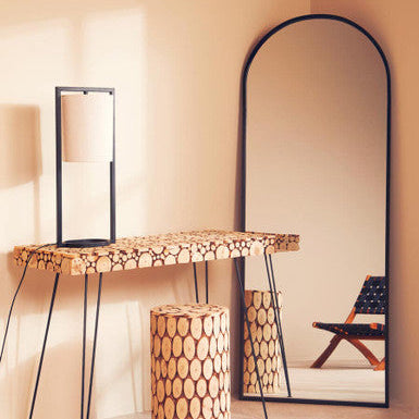 Wooden console table with patterned legs and stool against a beige wall with a large mirror.