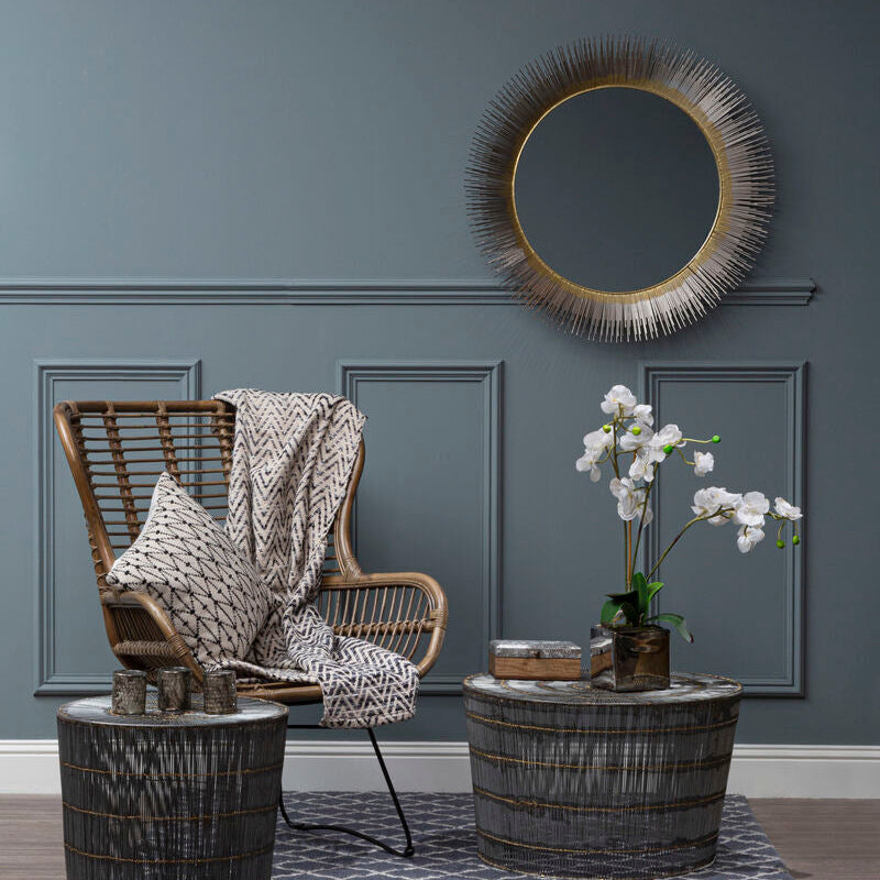 Living room with wicker chair, round mirror, and decorative elements on a gray wall.