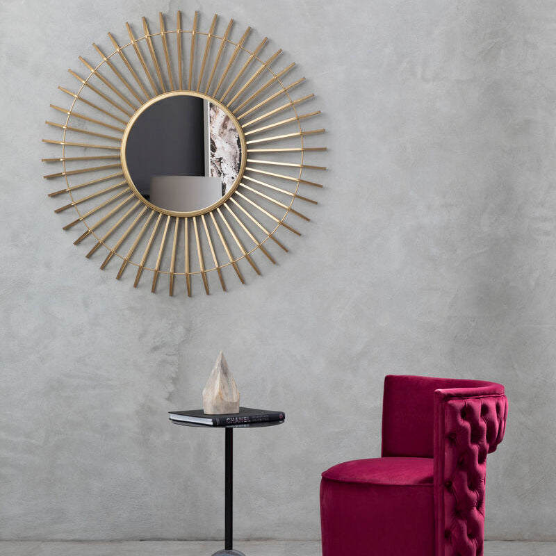 Decorative gold mirror on a gray wall with a pink chair and small table below.