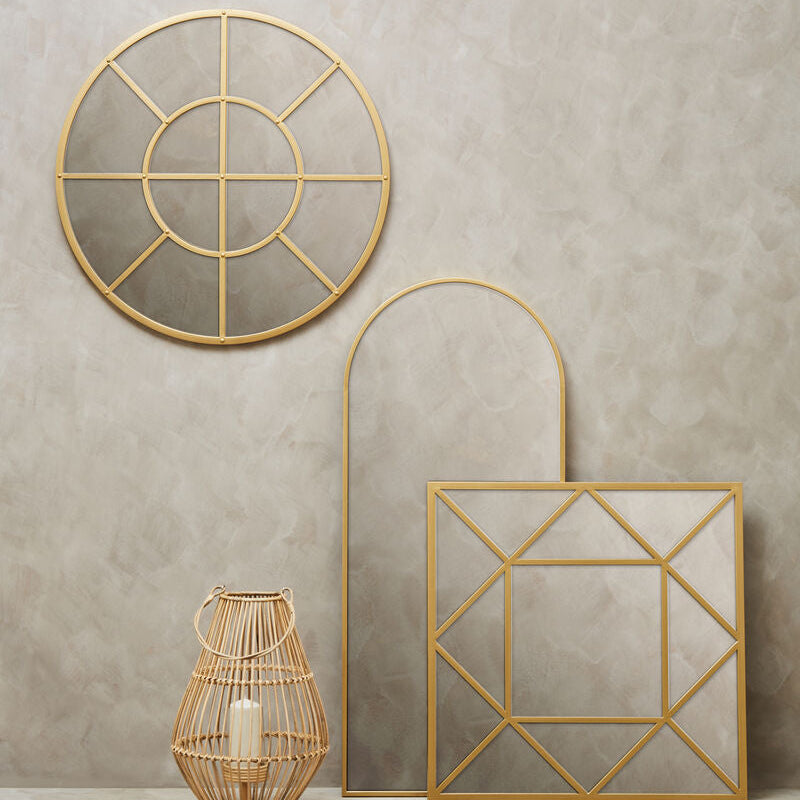 Three gold geometric mirrors on a beige wall with a woven basket and candle.