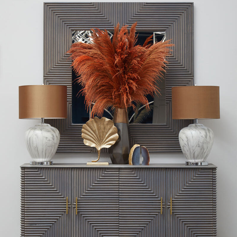 Decorative console table with lamps, plant, and decorative items against a textured wall.