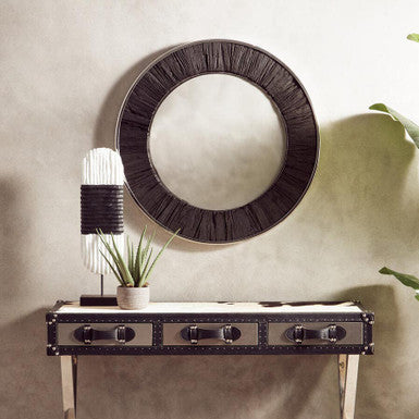 Decorative console table with round mirror and lamp against a beige wall.