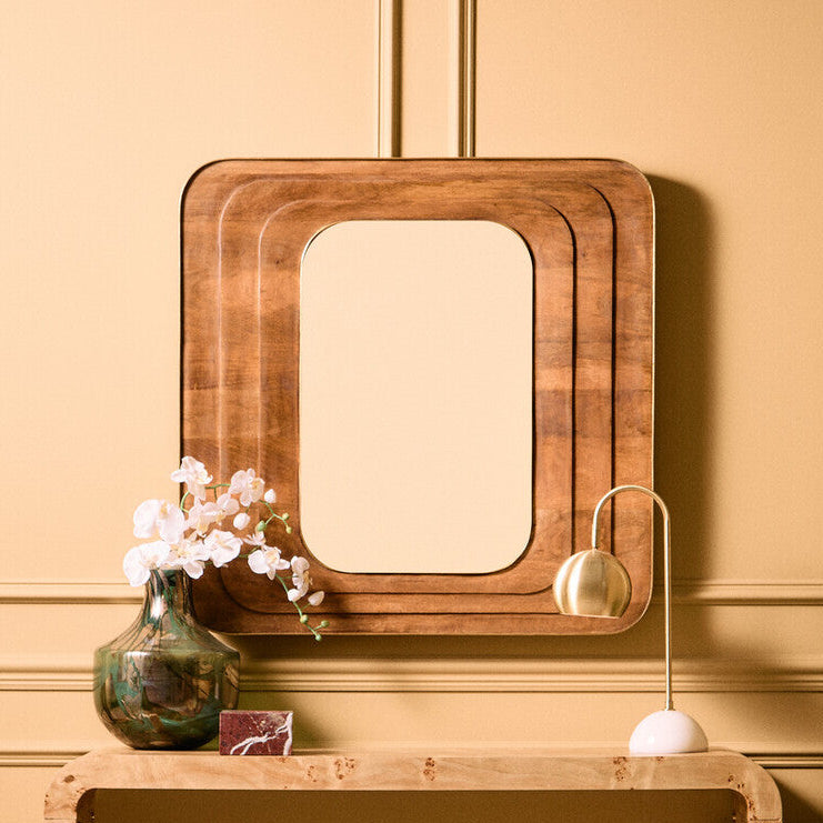 Wooden console table with mirror and decorative items against a beige wall.