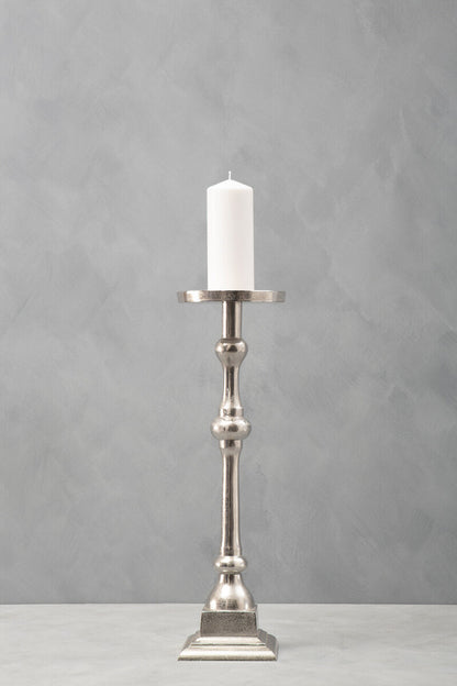 Silver candle holder with a white candle on a gray background
