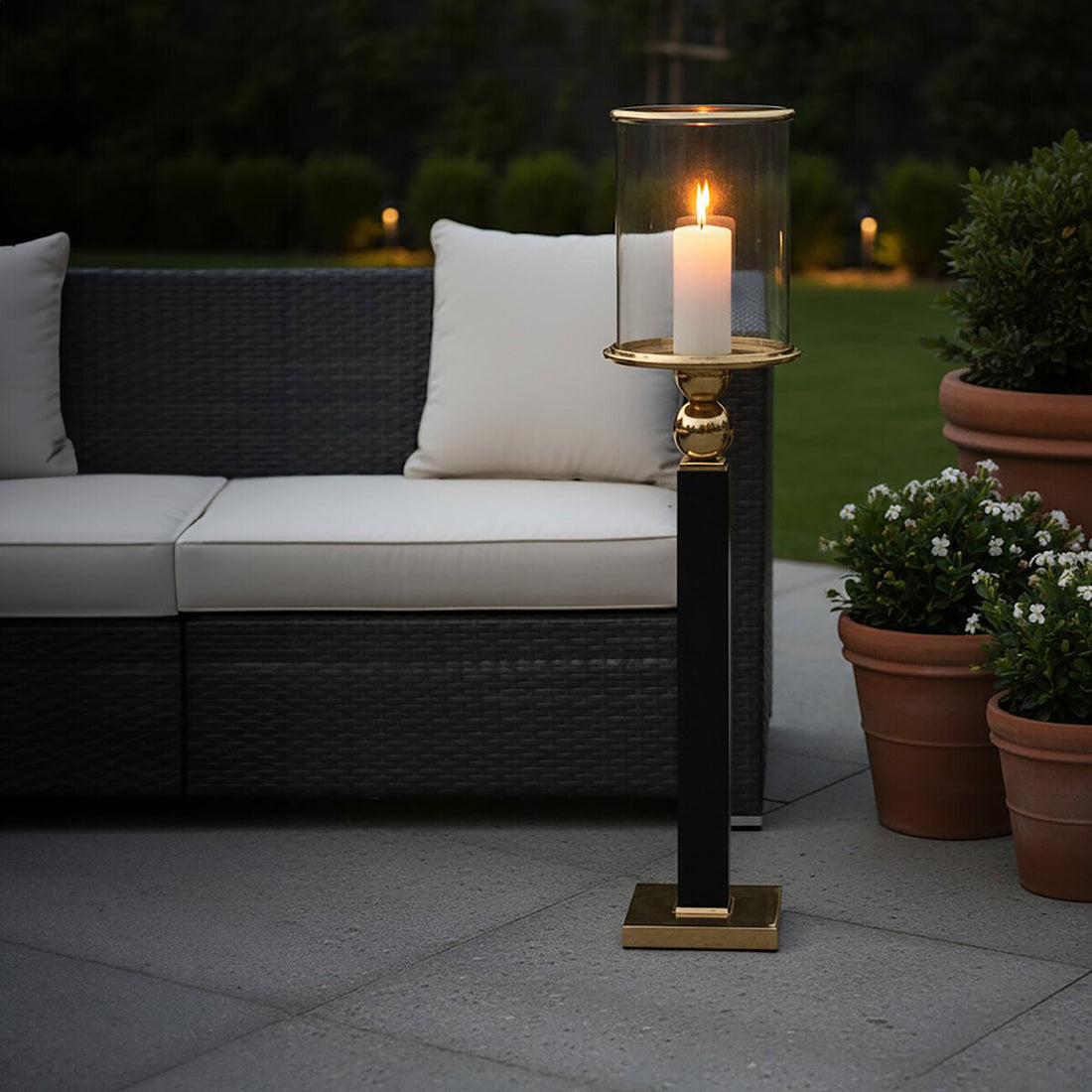 Outdoor patio scene with a candlelit lantern, sofa, and potted plants.