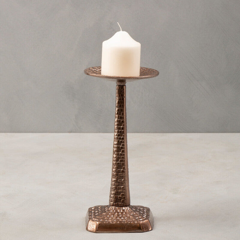 Bronze candle holder with a white candle on a gray background