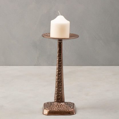Bronze candle holder with a white candle on a gray background