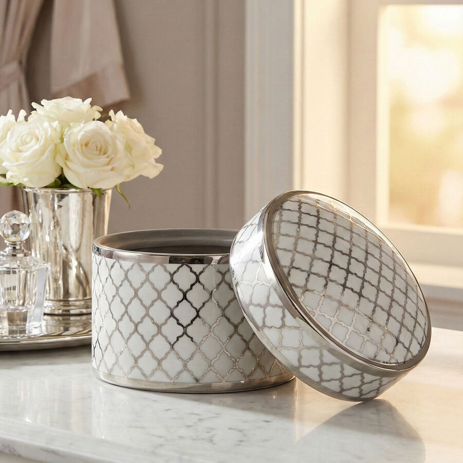 Decorative ceramic containers with a geometric pattern on a marble surface, with a vase of white flowers in the background.