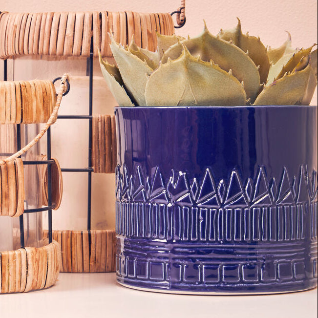 Blue textured planter with a succulent on a white surface, with two wooden lanterns in the background.