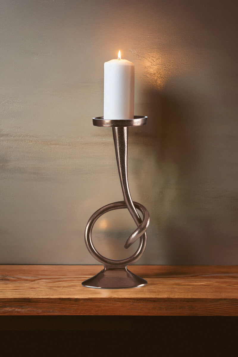 Decorative candle holder with a lit candle on a wooden surface and brown background