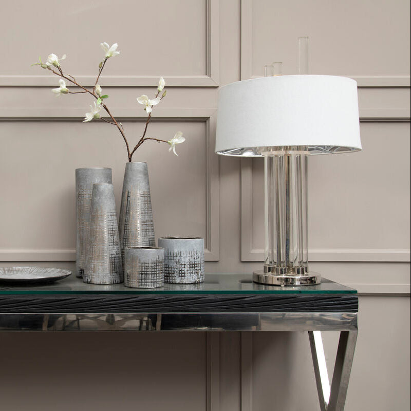 Decorative table setting with lamps, vases, and a plate on a reflective surface.