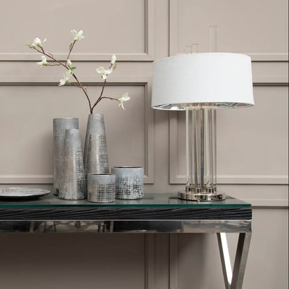 Decorative table setting with lamps, vases, and a plate on a reflective surface.