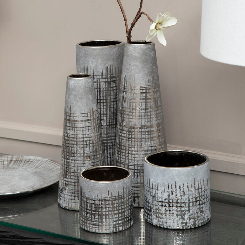 Set of four gray textured vases with white flowers on a reflective surface.