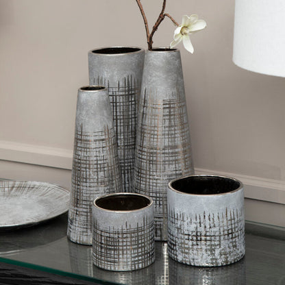 Set of four gray textured vases with white flowers on a reflective surface.