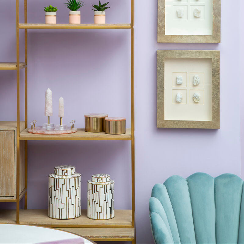 Decorative shelf with plants and candles against a purple wall with framed pictures.