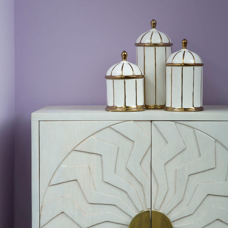 Decorative jars with gold accents on a white cabinet against a purple wall