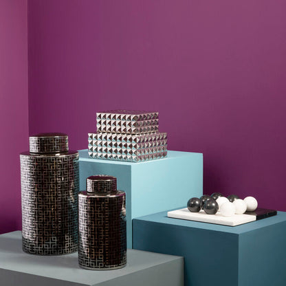 Decorative vases and sculptures on geometric platforms against a purple wall