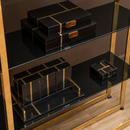 Black decorative boxes with gold accents on a black shelf with gold legs.