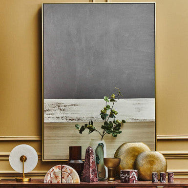 Decorative setting with a framed abstract painting on a wall, wooden cabinet with decorative items, and gold accents.