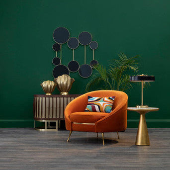 Modern interior with an orange chair, gold side table, and decorative wall art against a green wall.