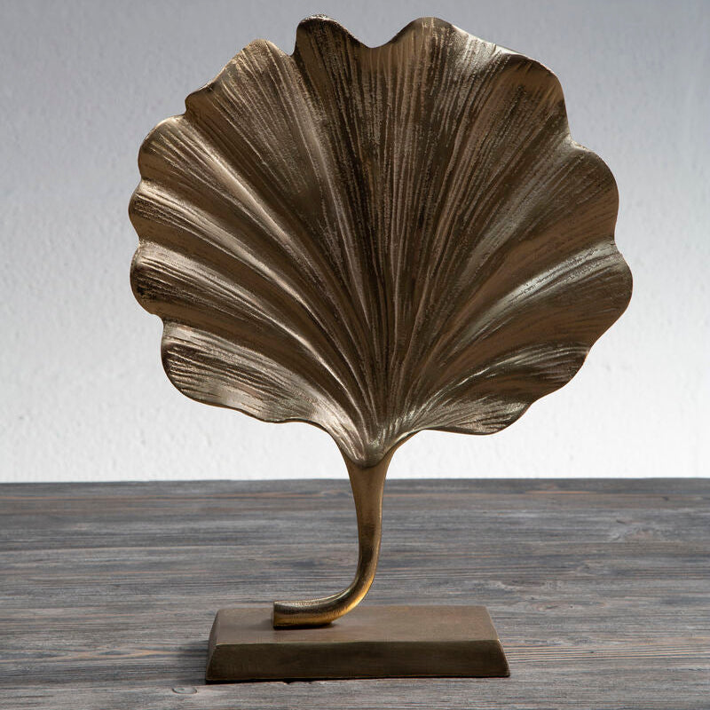 Bronze leaf-shaped sculpture on a wooden surface with a gray background