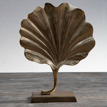 Bronze leaf-shaped sculpture on a wooden surface with a gray background