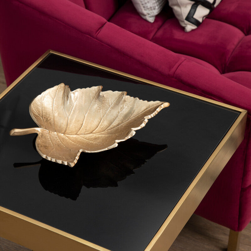 Gold leaf-shaped tray on a black square table with a red sofa in the background