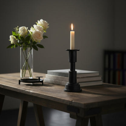 Candle in a black holder on a stack of books with white roses in a vase on a wooden table.