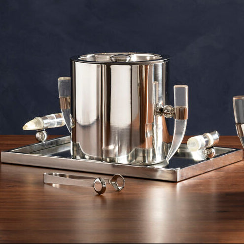 Set of silver kitchenware including a pitcher, pot, and bowl on a wooden surface with a dark background.