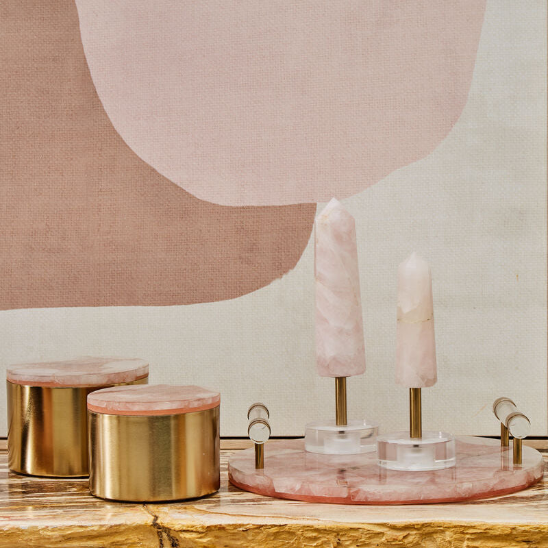 Decorative setup with gold candle holders and pink candles on a wooden table against a abstract wall.