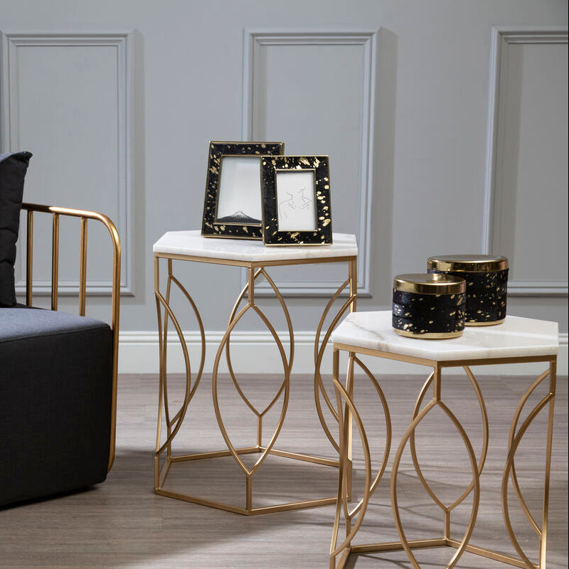 Modern black chair with gold frame and two marble tables with decorative items in a room.