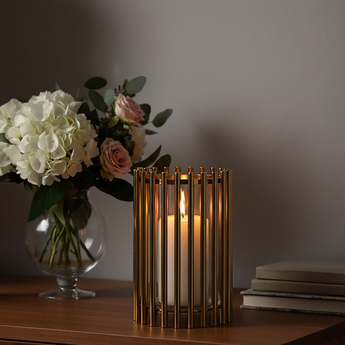 Candle in a decorative holder with flowers and books on a wooden surface