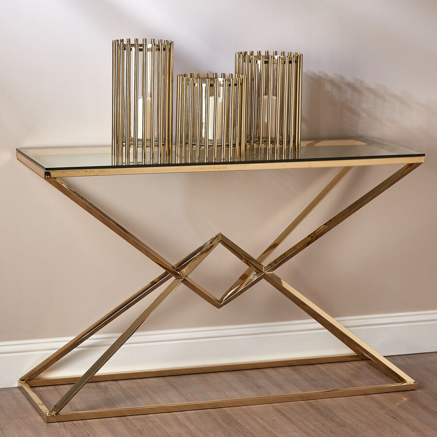 Gold console table with glass top and decorative vases against a beige wall.