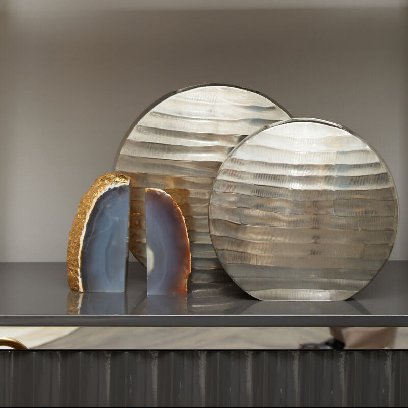 Decorative items including metallic plates and sculptures on a shelf against a neutral wall.