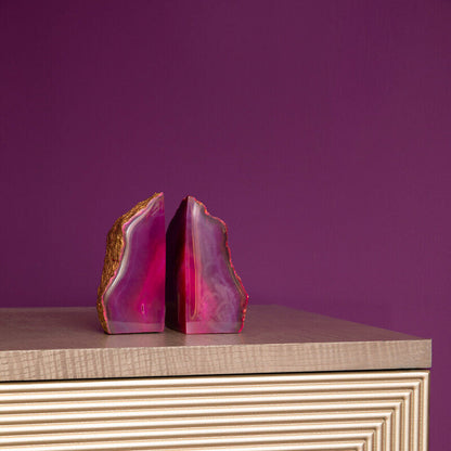 Pink agate bookends on a textured surface with a purple background