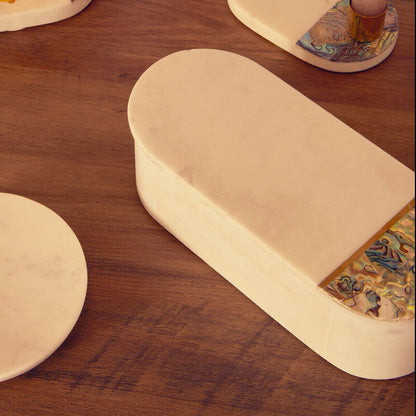 Decorative items including a cylindrical box, coasters with artistic designs, and a small cup on a wooden surface.