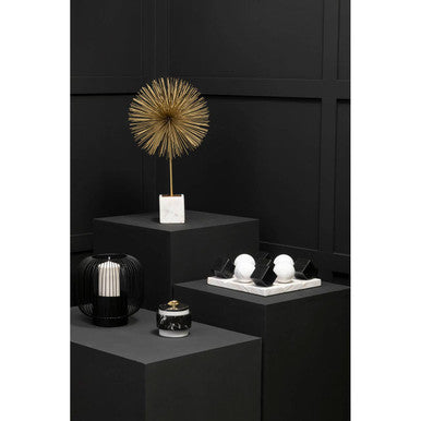 Decorative items including a gold sculpture, candles, and a vase on black stands against a black background.