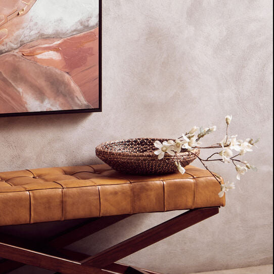 Abstract art piece on a wall above a brown leather bench.