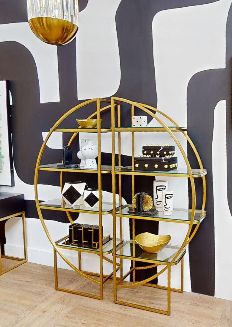 Gold circular shelving unit with decorative items against a black and white abstract wall.