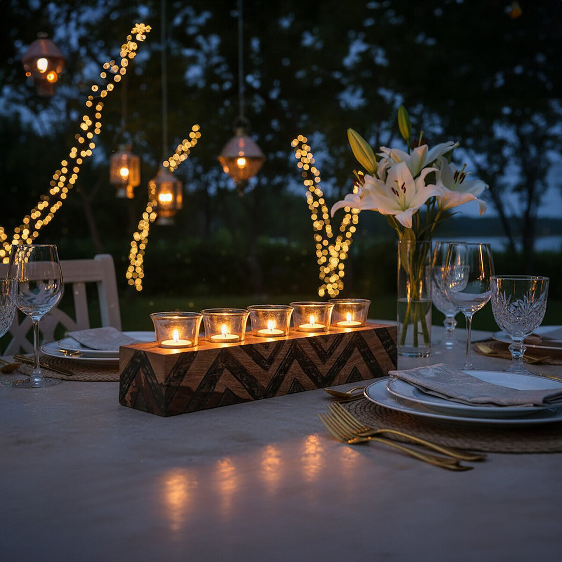 Dining table set with candles, flowers, and glasses at night with string lights in the background.
