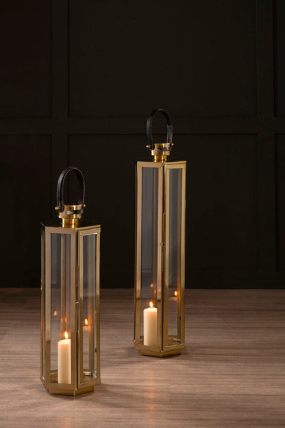Two brass lanterns with candles inside on a wooden floor against a dark paneled wall.