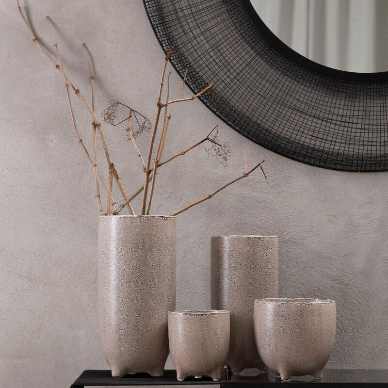 Set of gray ceramic vases on a black console table with a round mirror in the background.