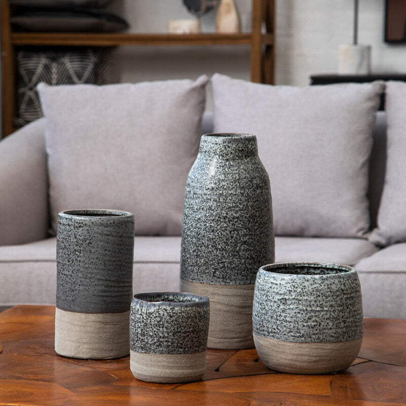 Set of four textured vases on a wooden table with a gray sofa and bookshelf in the background.