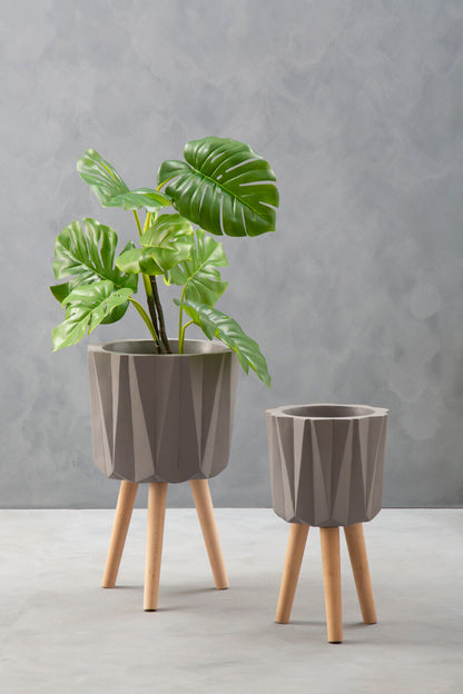 Two gray planters with wooden legs on a light gray surface against a gray wall.