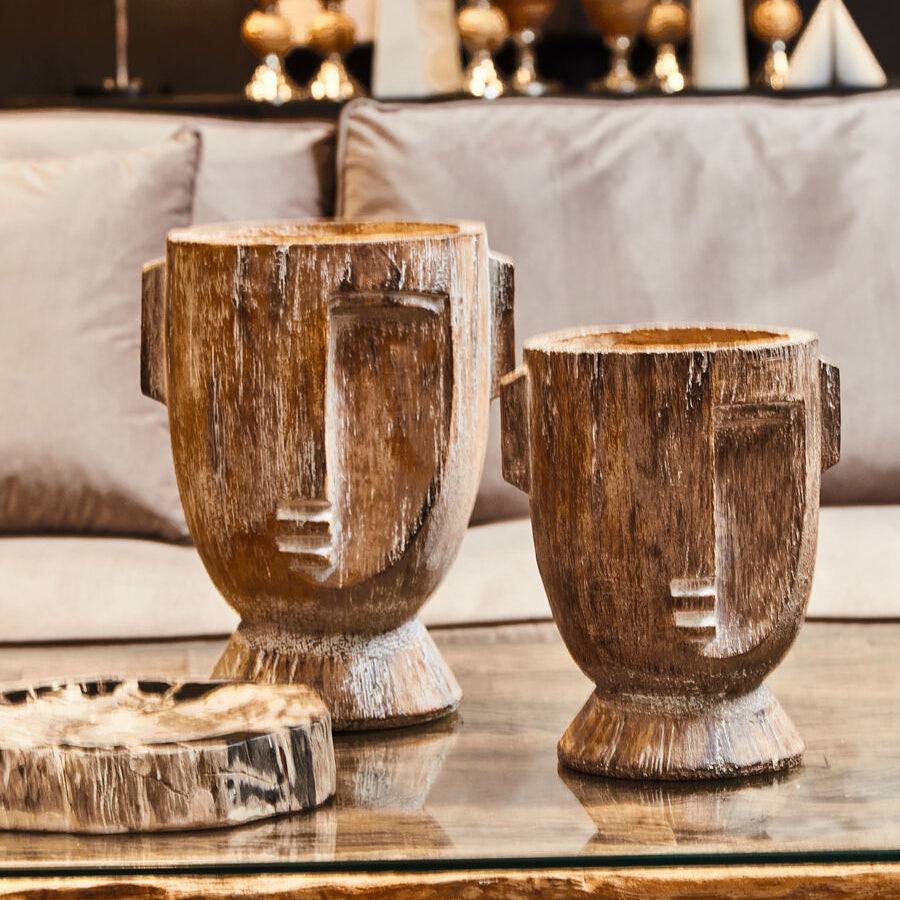 Two wooden urns on a glass table with a blurred background of decorative items.