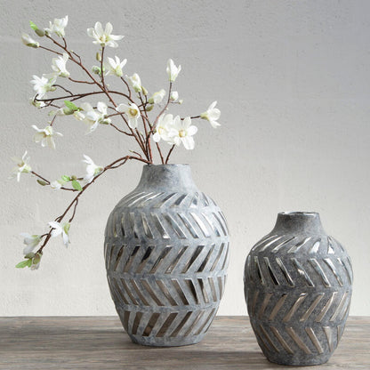 Two gray textured vases with a branch of white flowers on a wooden surface.