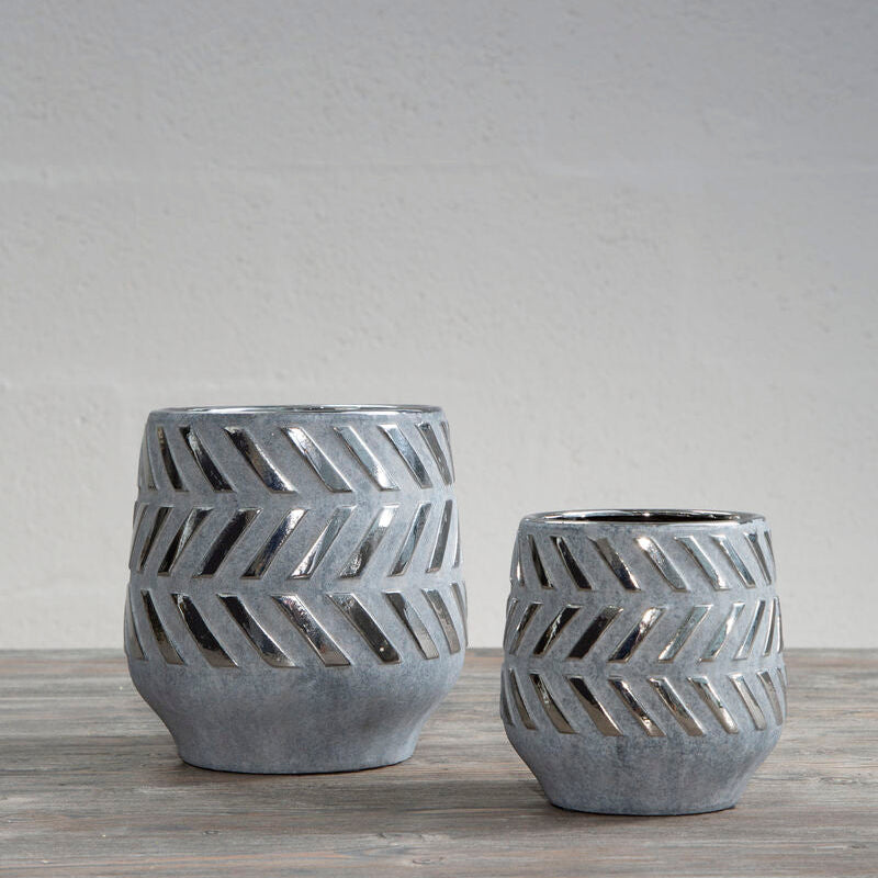 Two gray ceramic planters with geometric patterns on a wooden surface and gray background