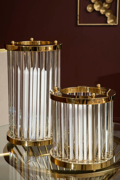 Two cylindrical glass containers with gold accents on a reflective surface.
