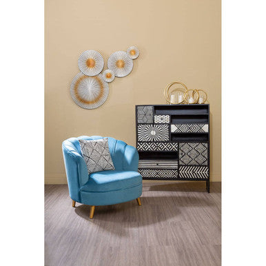 Blue armchair in a room with decorative wall art and a black and white patterned cabinet.