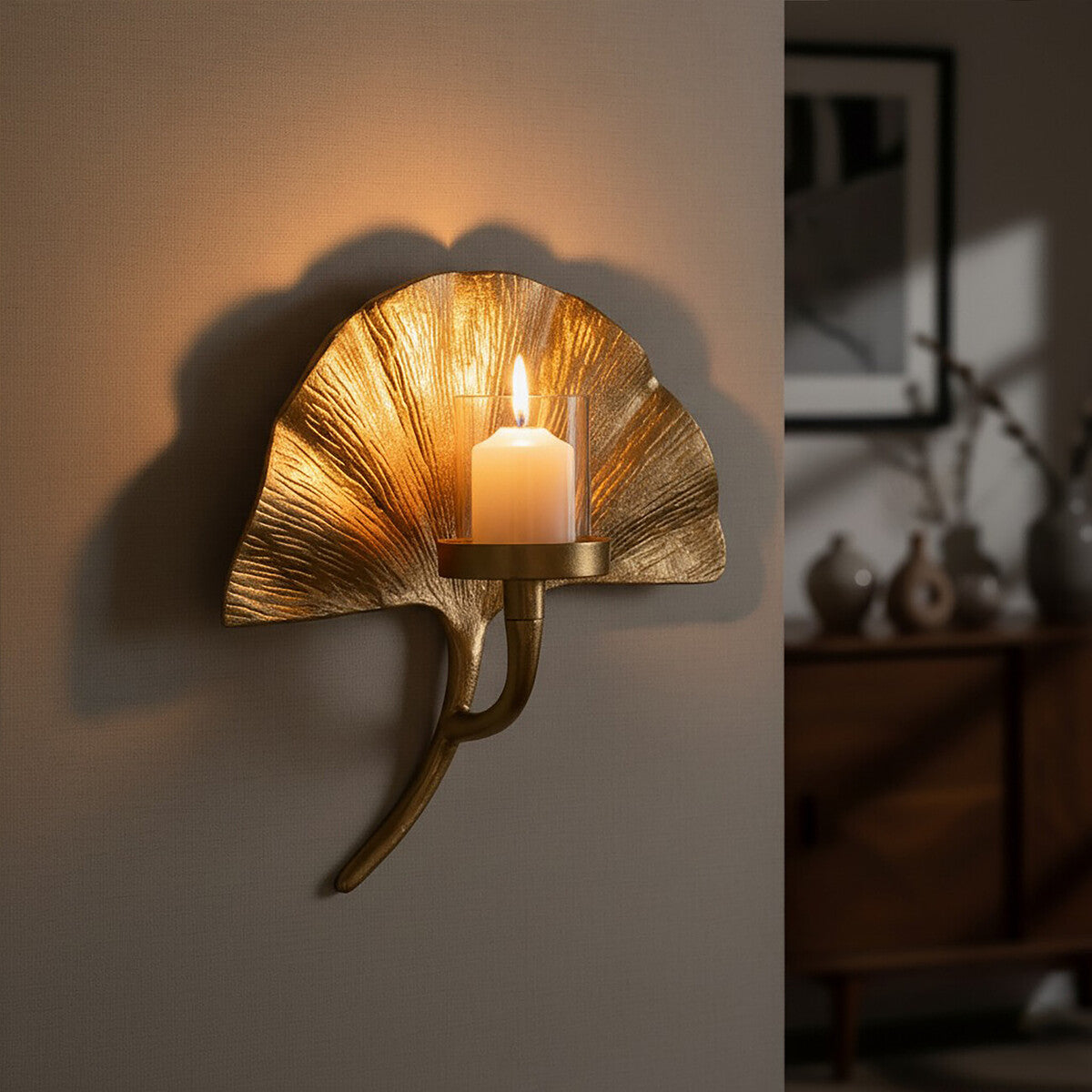 Gold wall sconce with a lit candle on a neutral wall